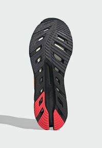 Black and red athletic shoe sole features a patterned tread, rubber material, and drainage holes for grip and flexibility.
