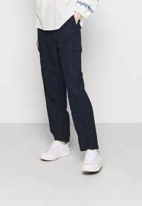 Granatowe spodnie cargo o prostym kroju, z bocznymi kieszeniami i gładką teksturą, zestawione z białymi trampkami i jasnym topem.