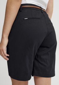 Shorts noirs avec une coupe ajustée, arborant une ceinture marron, une poche arrière avec des éléments en métal argenté, et un tissu en coton lisse.
