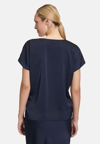 Blusa in satin bleu navy con vestibilità rilassata, maniche corte e scollo ampio, caratterizzata da una texture liscia e un design minimalista.