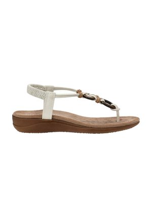 Sanda blanca con tiras, equipada con una plantilla acolchada, que presenta detalles trenzados en beige y negro, y una suela flexible de goma marrón. Diseño plano.