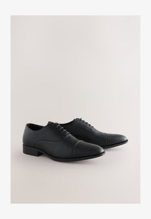 Black leather dress shoes with a smooth finish, laced design, rounded toe, and a low block heel. Features a textured body and cap toe detail.
