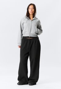 Γκρι φούτερ με φερμουάρ και κουκούλα, συνδυασμένο με μαύρο παντελόνι φαρδύ. Μαλακό ύφασμα, ριμπ μανσέτες και ελαστική μέση.