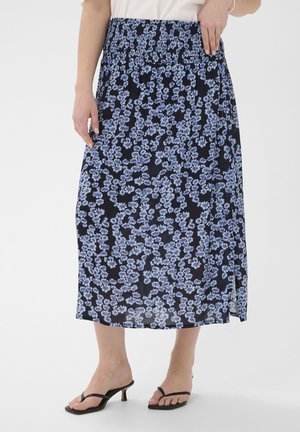 Frau trägt einen marineblauen Midi-Rock mit hellblauem Blumendruck, elastischem Bund, seitlichem Schlitz, weißem Oberteil und schwarzen Sandalen mit Absatz.