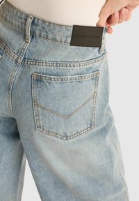 Jasnoniebieskie dżinsy o luźnym kroju, z dwoma tylnymi kieszeniami z detali w szewron i markową czarną skórzaną łatą na wysokości talii.