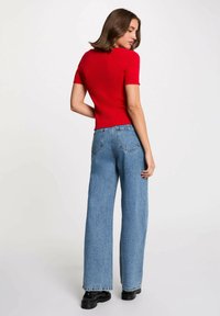 Top corto a righe rosso con bordi scallop, abbinato a jeans azzurri a vita alta e gamba larga e scarpe chunky nere.