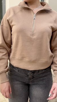 Beige színű, cipzáras pulóver magas gallérral, raglán ujjakkal és bordázott alsó résszel. Sötét farmernadrággal párosítva, amelyen két gomb díszítés található.