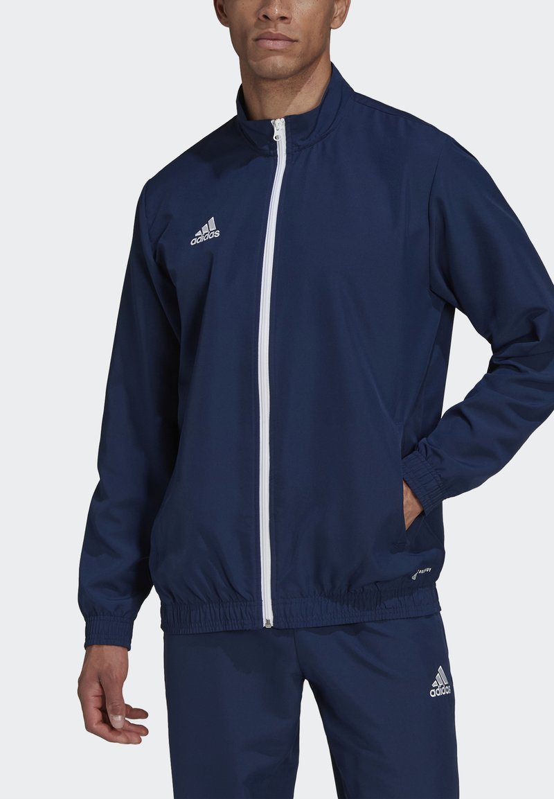 Marineblauwe sportjack gemaakt van lichtgewicht stof, met een witte ritssluiting, elastische manchetten en zijzakken. Adidas-logo op de borst.