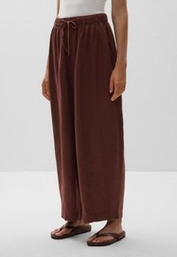 Wide-leg pants in a rich brown fabric, featuring an elastic waistband with a drawstring, side pockets, and a soft, textured finish.