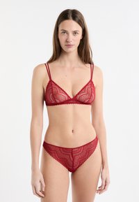 Conjunto de bralette de encaje rojo y braguita a juego, con bordes festoneados, tirantes delgados y una textura transparente en toda la prenda.