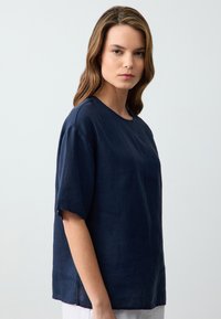 Maglietta in lino blu navy con vestibilità rilassata, maniche corte, scollatura rotonda e cuciture visibili lungo l'orlo.