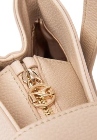 Interno di una borsa a tracolla in pelle beige con una cerniera dorata con un tirante logo, superficie testurizzata e dettagli di cucitura evidenti.