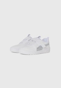 Des baskets Puma blanches avec deux bandes Velcro et des accents argentés sur un fond clair.