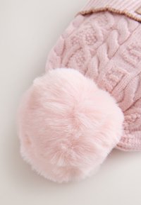 Lyserød strikket hue med kabelmønster, der har en stor, blød faux fur-pompon. Ribstrikket bånd øverst tilføjer en tekstureret detalje.