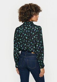 Camisa negra de manga larga con un patrón abstracto en verde y azul, con cuello estructurado y puños abotonados. Combinada con jeans azul oscuro.