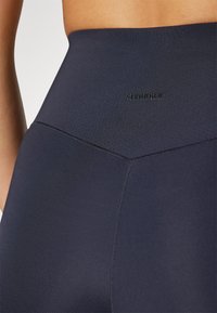 Tengerészkék, magas derékú leggings sima, rugalmas anyagból, fekete dombornyomott "STRONGER" logóval és varrási részletekkel a letisztult megjelenés érdekében.