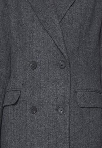 Dubbelzijdige grijze visgraatcoat met een gestructureerde stof, zwarte knopen en twee voorzakken.