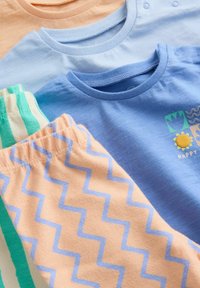 Trois bodies pour bébé pliés en pêche, bleu clair et bleu, accompagnés d'un pantalon pêche à motif zigzag et d'un pantalon rayé vert, présentés en gros plan.