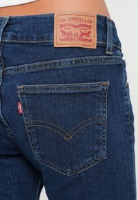 Mørkeblå denimjeans med et lædermærke fra Levi Strauss & Co. bagpå, med gule stikninger og et klassisk baglomme-design.