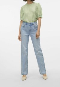 Top corto de manga corta texturizado en verde claro con un patrón de bordes en picos, combinado con jeans rectos de talle alto en azul claro y zapatos de tacón beige.