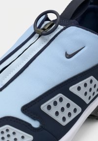 Svijetloplave slip-on tenisice s tamnoplavim naglascima, s patentnim zatvaračem, teksturiranim preklopima s perforiranim detaljima i kružnim povlačnim držačem.