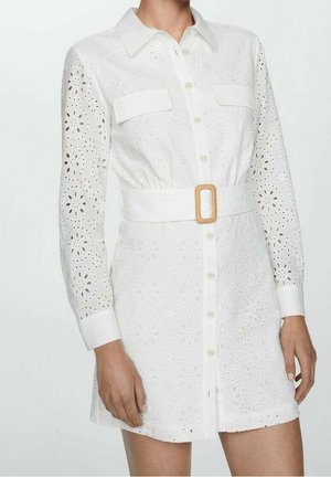 Biała sukienka z guzikami, z długimi rękawami z ażurowej koronki, dwoma kieszeniami na piersi i szerokim paskiem z prostokątną klamrą w talii.