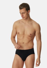 Zwarte katoen slip met een strak ontwerp, voorzien van een elastische tailleband en een gladde textuur, gepresenteerd op een mannelijke model.