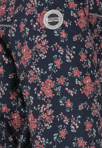 Marineblauwe legging van stof met een rood bloemenpatroon en groene accenten. Inclusief een cirkelvormig Zigzag-logo op de taille. Zachte, decoratieve textuur.
