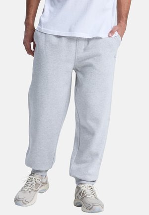 Gray cotton sweatpants with elastic waistband, side pockets, and tapered legs. Worn with light-colored sneakers. Simple and functional design.