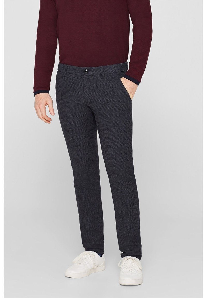 Donkergrijze op maat gemaakte broek van textuurstof met voorzakken en een knoopsluiting, gecombineerd met witte sneakers.