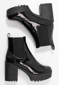 Botines de charol negro con un tacón alto y grueso, paneles laterales elásticos y una suela de goma texturizada. Acabado suave y detalles de costura en contraste.