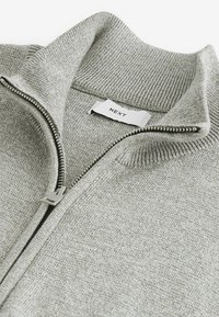 Hellgrauer Reißverschluss-Pullover mit geripptem Kragen und Bündchen, der eine glatte Textur aufweist und ein kleines Markenlabel "NEXT" in der Nähe des Reißverschlusses hat.