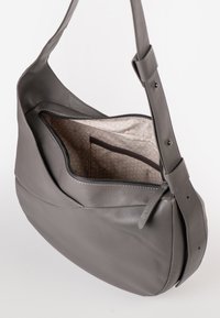 Graue Leder-Schultertasche mit verstellbarem Schulterriemen, oberer Reißverschluss geöffnet, der das gemusterte beige Stoffinnere und eine Innentasche zeigt.