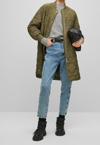 Matlad olivgrön lång jacka, grå tröja, ljusblå raka jeans och svarta snörstövlar; har ribbad mudd och bälte i midjan.