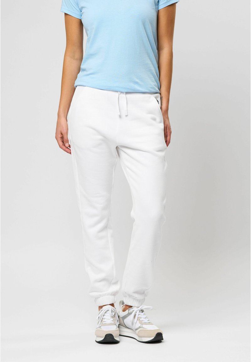 Hvide sweatpants med elastiske manchetter og talje, parret med en lyseblå t-shirt og hvide sneakers med grå detaljer.