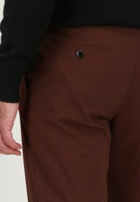 Pantalons marron en tissu texturé semblable à de la laine, dotés d'une poche arrière avec un accent de bouton noir. Stylés avec une silhouette ajustée et élégante.