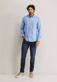Lichtblauw overhemd met lange mouwen, gecombineerd met donkerblauwe jeans en beige sneakers. Glad stofoppervlak, standaard kraag ontwerp.