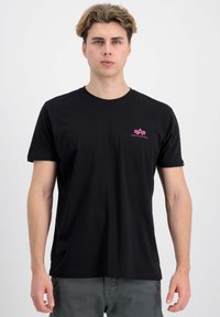 Musta lyhythihainen t-paita, jossa on vaaleanpunainen logo rinnassa, valmistettu pehmeästä kankaasta, jossa on klassinen pyöreä kaula-aukko ja tavallinen istuvuus.