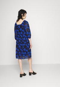 Vestido azul com padrão floral, mangas três quartos, cintura ajustada e saia fluida. Combinado com mules pretas de salto.