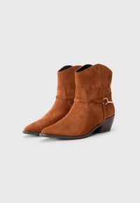 Bottines en suède marron à bout pointu, avec un petit talon empilé et une sangle décorative avec un détail en métal doré.
