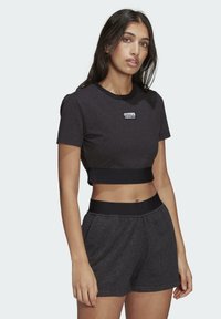 Svart crop top och matchande shorts gjorda av mjuk bomull. Har en rund halsringning, korta ärmar och en framträdande varumärkeslogotyp på bröstet.