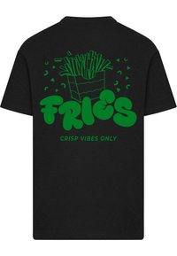 Musta t-paita, jossa on vihreä graafinen kuva ranskalaisista perunoista niiden sisältävästä laatikosta. Kuvassa on tyyliteltyjä ranskalaisia perunoita ja teksti, joka sanoo "VAAN CRISP VIBES RANSKAISILLE PERUNOILLE" paksulla fontilla.