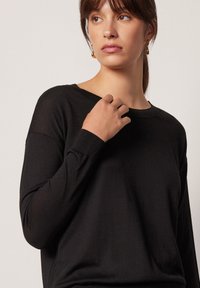 Svart långärmad tröja i mjukt material, med bred rund halsringning och avslappnad passform, samt ribbade ärmslut och nederkant.