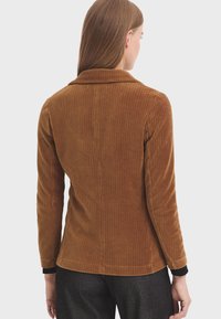 Braune Cordjacke mit Kragen, langen Ärmeln und vertikaler gerippter Textur. Enthält ein kontrastierendes schwarzes Manschettendetail.