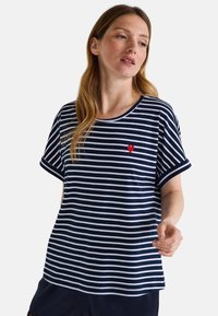 T-shirt rayé bleu marine et blanc avec des manches courtes à revers, un col rond, et une petite broderie en forme de cœur rouge sur la poitrine. Matière en coton.