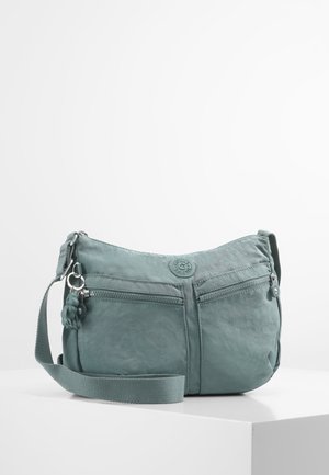 Sac bandoulière bleu clair avec sangle réglable, deux poches avant zippées et un petit porte-clés en forme de singe attaché au tirette du zip.