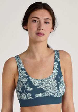 Teal sportbh met een wit paisleypatroon, brede banden en een gladde textuur. Het ontwerp bedekt de voorkant en de zijkanten.