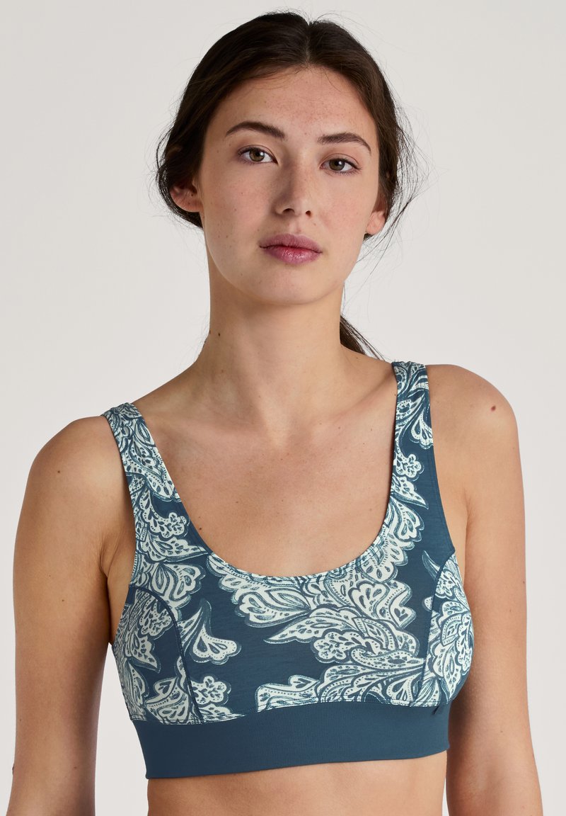 Teal sportbh met een wit paisleypatroon, brede banden en een gladde textuur. Het ontwerp bedekt de voorkant en de zijkanten.