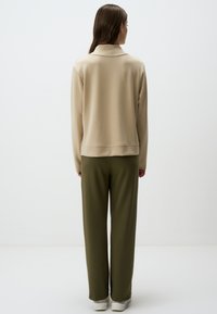 Pullover in pile beige con colletto alto, abbinato a pantaloni a gamba larga verde oliva. Il design è semplice con una texture liscia.