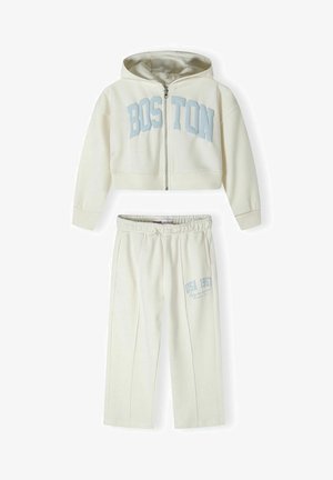 Krém színű, két részes otthoni viselet szett, amely zipzáras kapucnis pulóverből és a "BOSTON" felirattal ellátott összeillő nadrágból áll, amelyen a "USA 1967" grafikai részlet található.